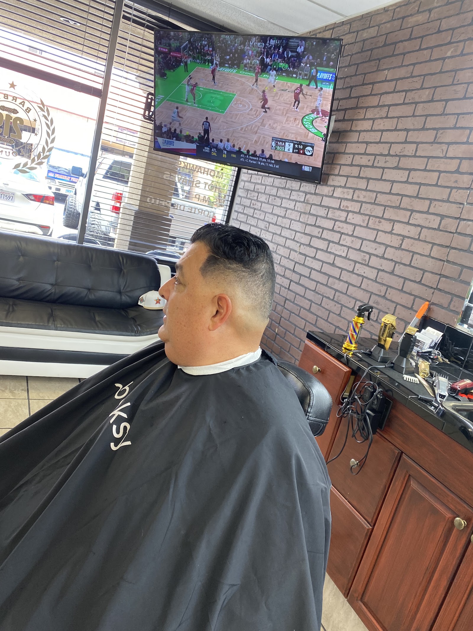 Man with a fresh fade haircut seated in a barber chair watching TV
