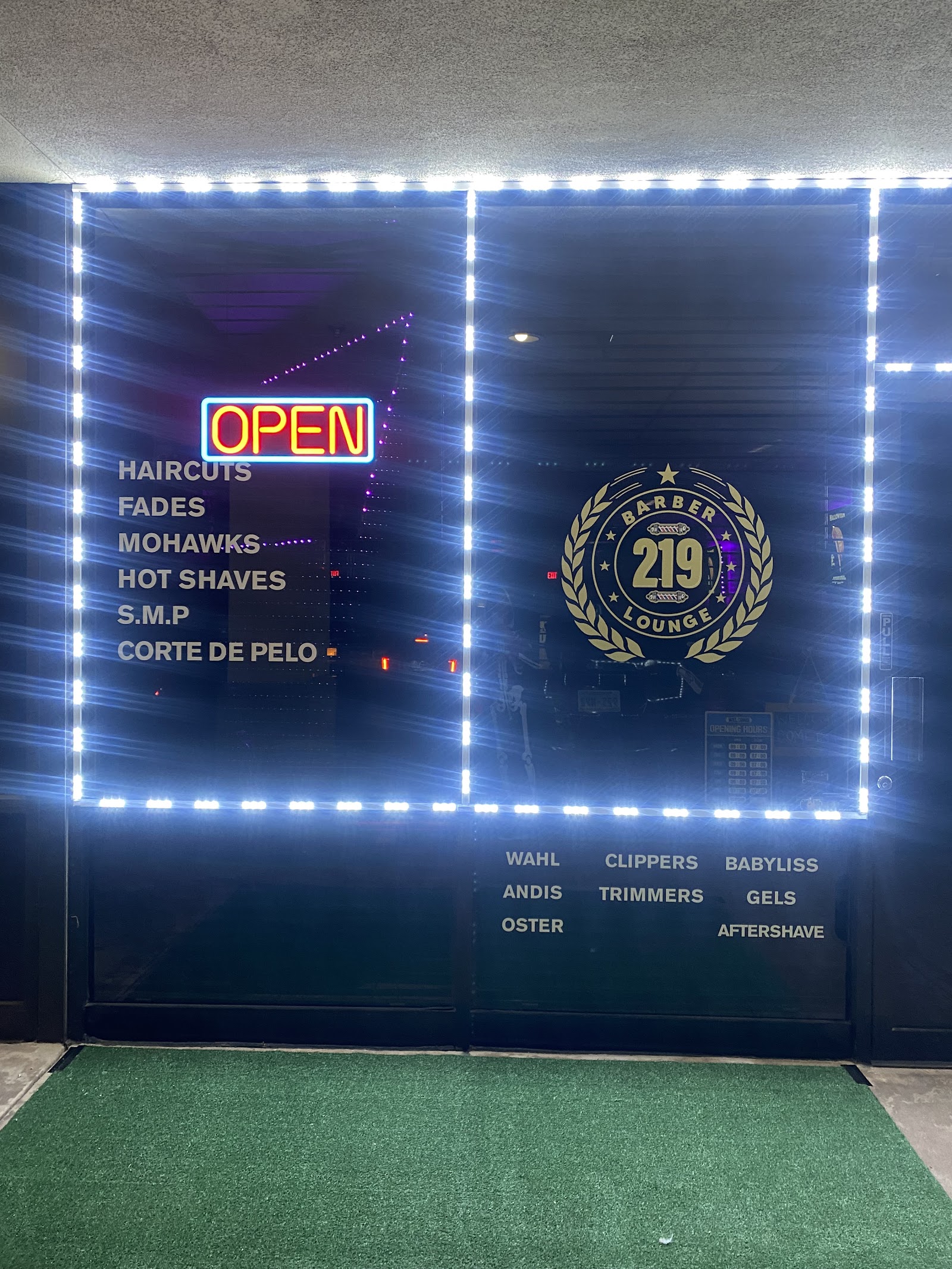 Storefront window at night with OPEN neon sign and a list of services